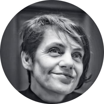 A black and white headshot of a woman in her early fourties with small studded earings and wavy fringe hair smiling at something in the distance